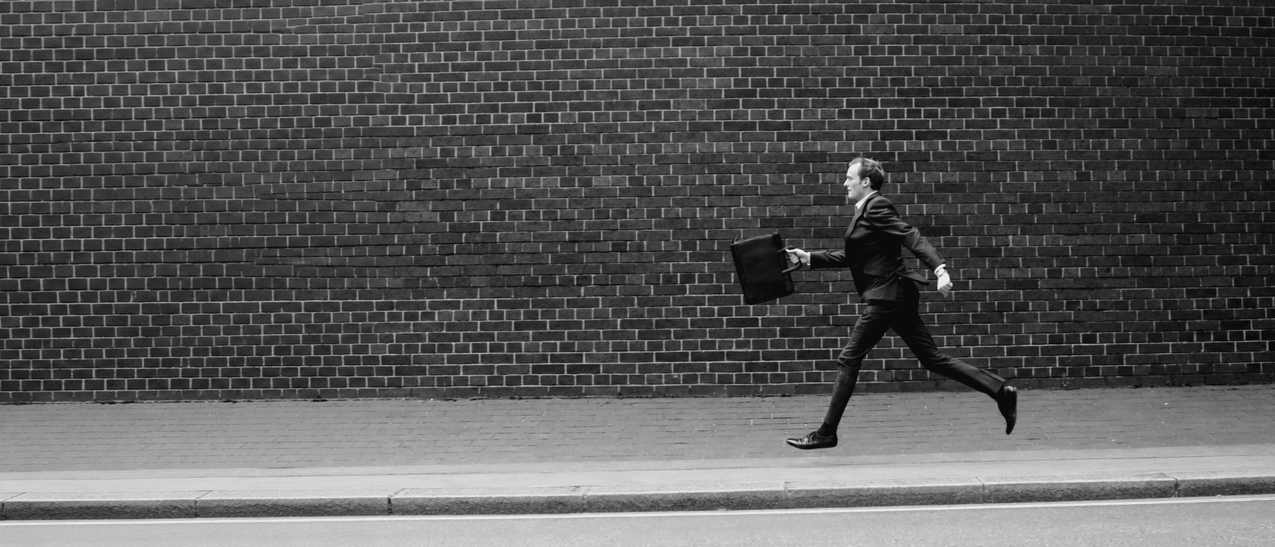 A professional running with a briefcase alongside a brick wall